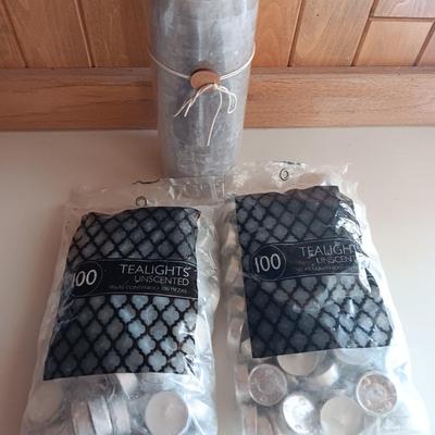 Two unopened bags of 100 ea. unscented tea light candles and a decorative pillar candle