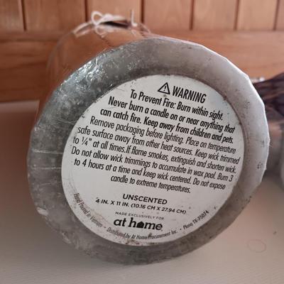 Two unopened bags of 100 ea. unscented tea light candles and a decorative pillar candle