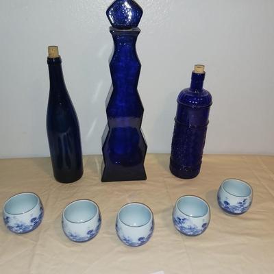 3 BLUE GLASS BOTTLES WITH 5 SIGNED PORCELAIN CUPS