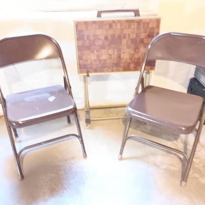 Two brown metal folding chairs and a set of 4 retro TV trays on organizing / storage cart.