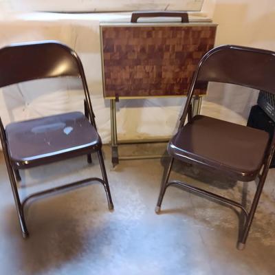 Two brown metal folding chairs and a set of 4 retro TV trays on organizing / storage cart.