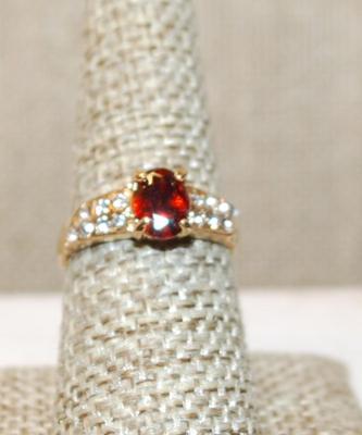 Size 8 Cranberry Red Oval Cut Stone Ring with 7 Clear Stones Each Side Accents on a Gold Tone Band (2.8g)