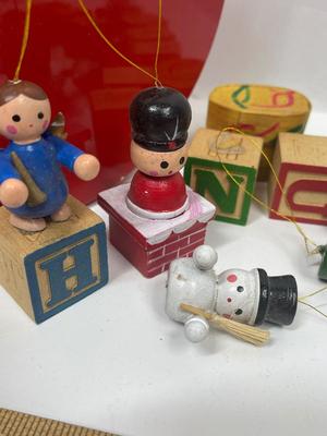 Sale Photo Thumbnail #615: 10 ornaments created bt attaching wooden baby blocks to wood figurines or other objects.  Also included is a small lidded box with miniature Guatemalan Worry Dolls. All inside a red, round tin.  Good condition, some of the blocks have come unglued from th