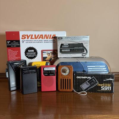 LOT 104: Transistor Radios, Sylvania Portable DVD Player, Olympus Pearlcorder, Am/Fm Cordless Portable Alarm Clock Radio
