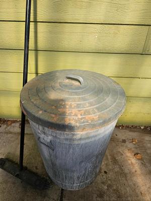 Galvanized metal trash can with lid and a push broom