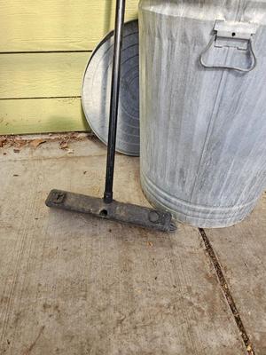 Galvanized metal trash can with lid and a push broom