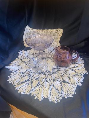 PURPLE PEDESTAL DISH, PITCHER, FOOTED CRYSTAL DISH AND DOILIES