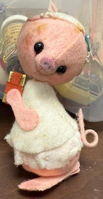 Sale Photo Thumbnail #293: Analee-style pig ornament, likely vintage, featuring a round, pink face with black button eyes and a stitched snout. It has a white, layered dress with a pink patch on its arm and a curly tail. Approx. 4" tall, in good condition.