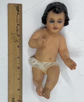 Sale Photo Thumbnail #67: Recling Statue made of hand-painted porcelain with varying flesh tones. It has glass eyes and open mouth.  Cradle has straw and blanket along with a gray scarf.