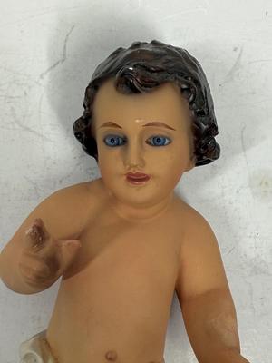 Sale Photo Thumbnail #71: Recling Statue made of hand-painted porcelain with varying flesh tones. It has glass eyes and open mouth.  Cradle has straw and blanket along with a gray scarf.