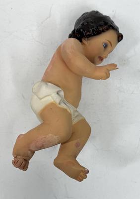 Sale Photo Thumbnail #69: Recling Statue made of hand-painted porcelain with varying flesh tones. It has glass eyes and open mouth.  Cradle has straw and blanket along with a gray scarf.
