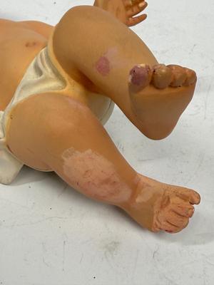 Sale Photo Thumbnail #70: Recling Statue made of hand-painted porcelain with varying flesh tones. It has glass eyes and open mouth.  Cradle has straw and blanket along with a gray scarf.