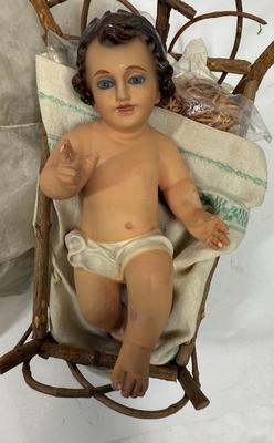 Sale Photo Thumbnail #65: Recling Statue made of hand-painted porcelain with varying flesh tones. It has glass eyes and open mouth.  Cradle has straw and blanket along with a gray scarf.