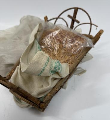Sale Photo Thumbnail #68: Recling Statue made of hand-painted porcelain with varying flesh tones. It has glass eyes and open mouth.  Cradle has straw and blanket along with a gray scarf.