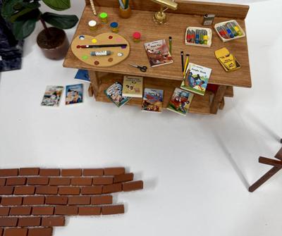 Sale Photo Thumbnail #329: Fireplace, 2 potted plants. brick patch, Miniaturized Disney Books, Miniaturized Disney Poster, Brass Light fixture on desk, scissors, brush, pencil, pain pallet, paint, chalk, crayons, newspapers etc
