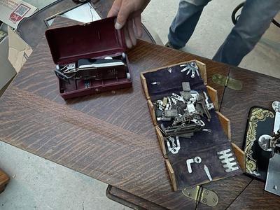 Sale Photo Thumbnail #787: Antique Singer Sewing Machine Table Plus Sewing Accoutrements (Lot of 4). Sewing machine with original table and foot pedal, cast iron and wood details. Also includes folding wooden box of different sewing feet, Singer buttonhole making foot, and pin cush