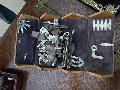 Sale Photo Thumbnail #788: Antique Singer Sewing Machine Table Plus Sewing Accoutrements (Lot of 4). Sewing machine with original table and foot pedal, cast iron and wood details. Also includes folding wooden box of different sewing feet, Singer buttonhole making foot, and pin cush