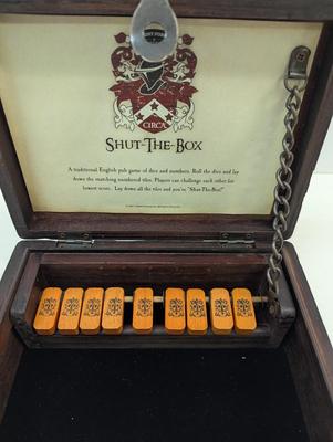Sale Photo Thumbnail #1546: The Shut-the-Box game by GAME is a traditional game that involves rolling two dice and covering the corresponding numbers on a wooden board. Players take turns rolling the dice and trying to shut the box by covering the corresponding numbers. The game is 