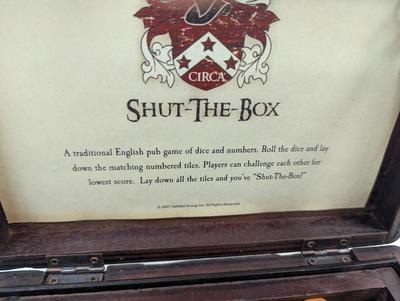 Sale Photo Thumbnail #1548: The Shut-the-Box game by GAME is a traditional game that involves rolling two dice and covering the corresponding numbers on a wooden board. Players take turns rolling the dice and trying to shut the box by covering the corresponding numbers. The game is 