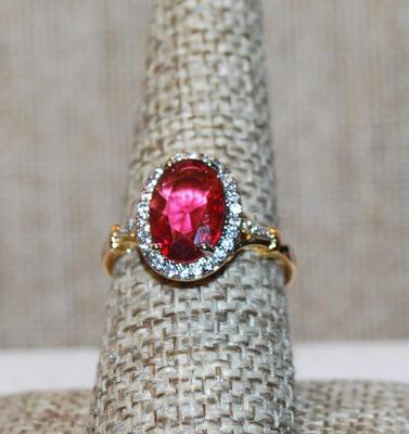 Size 8¼ Light Red Oval Cut Transparent Stone Ring with Full Clear Stones Surround and Side Accents on a Gold Tone Band (3.3g)