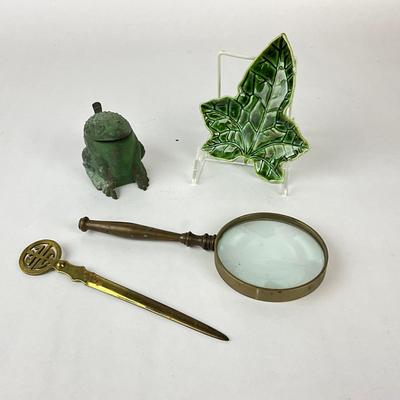 Sale Photo Thumbnail #1448: Comes with brass magnified glass, brass letter opener, frog ink well, leaf plate
Leaf plate is cracked twice (see photos)
Letter opener: 8" long
Mag. glass: 2.5" high x 4" diameter x 5.5" long
Leaf plate: 5" wide