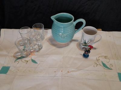 Blue pitcher with bee, coffee mug, metal rooster decor, and glasses with embroidered linen table runner