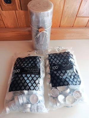 Two unopened bags of 100 ea. unscented tea light candles and a decorative pillar candle