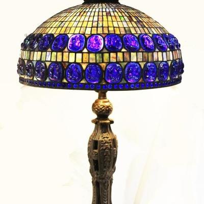 Very large metal lamp with stain glass shade. Base is brass with a bronze patina. ca. 1980. Blue glass stone like pieces reticulate the...