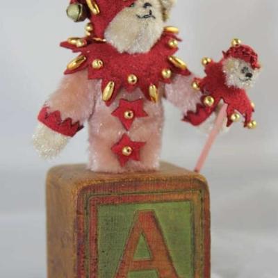 Jess-tee-200.  Tan Jester Bear on Antique Block  with Rose Body.  Wears a wine suede capelet with  gold beads.  A matching cap with bell....