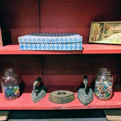 Marbles, cigar boxes, and antique irons on red bookcase