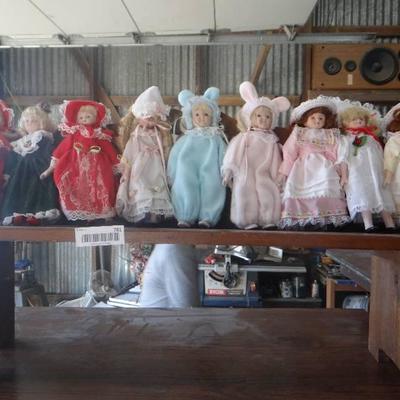 Lot of small porcelain dolls on wood bench.