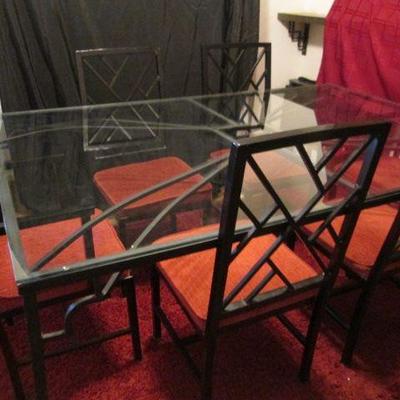 Black iron frame dining table and chairs, with a glass top and cushions of the seats
