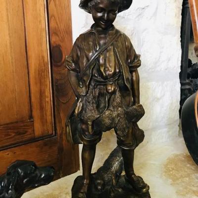 This beautiful bronze  sculpture features a bucolic young hunter dragging a rabbit in one hand, a small knapsack on his shoulder and two...