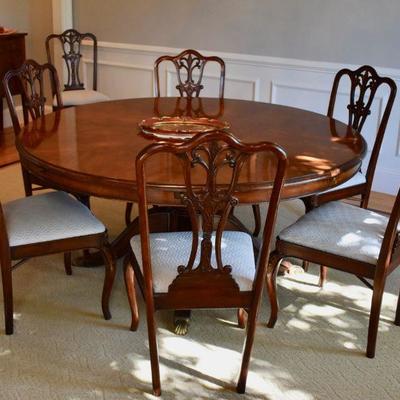 Round pedestal dining table with 10 chairs and additional leaves in storage cabinet