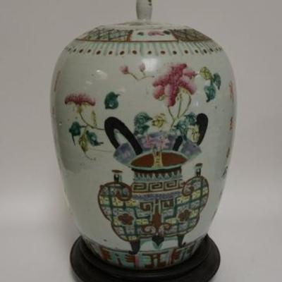 1022  HAND PAINTED ASIAN COVERED JAR DECORATED WITH URNS OF FLOWERS AND CALLIGRAPHY. SLIVER OFF THE FINIAL OF THE LID. HAS A WOODEN BASE....