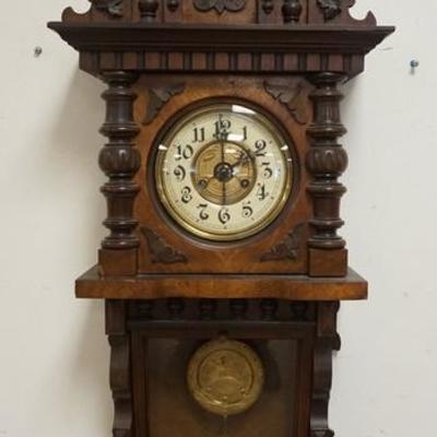 1158	CARVED WALNUT VICTORIAN WALL CLOCK. HAS EMBOSSED DESIGNS ON THE BRASS PENDULUM & FACE 16 1/2 IN WIDE X APPROXIMATELY 39 IN HIGH
