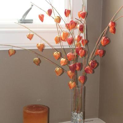 Orange Tone Pillar Candle on Wood Stand and Faux Orange Pod Floral Arrangement in Clear Cylindrical Glass Vase