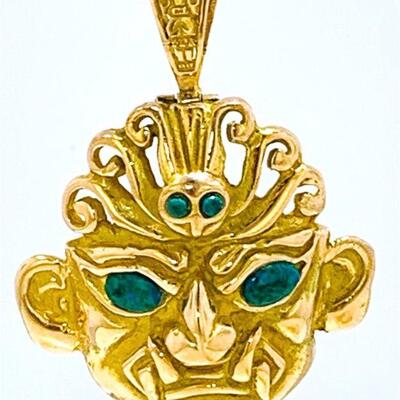 One 18kt gold tribal mask pendant. The pendant features two (2), bezel set, round cabochon green stones set in the center of the head...
