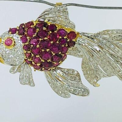 One 18kt two tone gold diamond & ruby brooch/pendant. The brooch has a fish motif featuring a body set with thirty-three (33), prong set,...