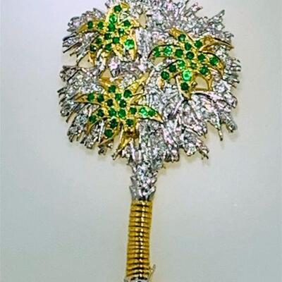 One 18kt two tone gold diamond & emerald palm tree brooch/pendant. The piece features eighty (80), pave set, round brilliant cut diamonds...