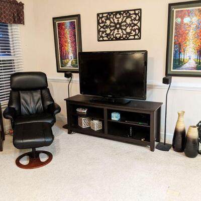 Shot of den showing 47" flatscreen tv, prints, wrought iron wall art, TV cabinet and black leather stressless recliner and ottoman