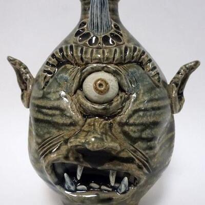 1164	GROTESQUE FACE JUG HAVING 1 HORN, 1 EYE AND OPEN MOUTH WITH EXPOSED TEETH. IMPRESSED SEA SHELLS AND DIE STAMPED DW ON HANDLE BASE,...