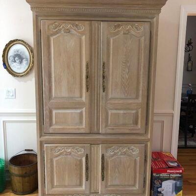 Whitewashed entertainment armoire with flower details and brass hardware. Stand for TV behind doors and bottom cabinets have storage...
