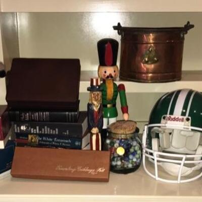 This lot contains a variety of books, some statues, Trivial Pursuit game with boomer pack, a Spartans football helmet, and a jar marbles....