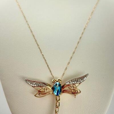 "A 14kt yellow gold dragonfly pendant with pin back. Central prong set oval shaped mixed cut natural blue topaz, approx. weight...