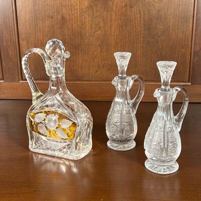 (3pc) CRYSTAL VESSELS | A pair of cut crystal oil and vinegar bottles with matching stoppers (h. 7-3/4 in.) and a medium sized crystal...