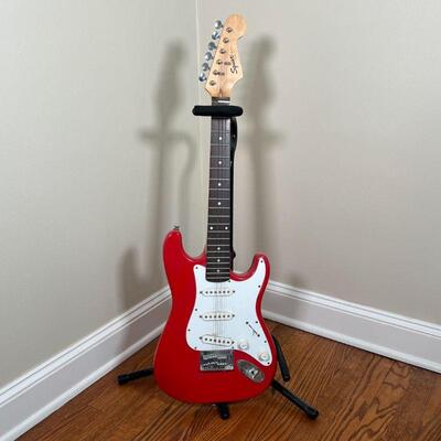 FENDER SQUIER ELECTRIC GUITAR | Red and white guitar on an On-Stage Stand (guitar h. 34-1/2 in.) [missing a few strings, can be cleaned]