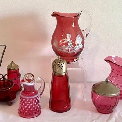 Variety of Vintage Cranberry Glass Items. Includes Mary Gregory Pitcher, Cranberry coin dot pitcher, cruet set and more.