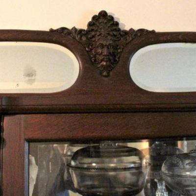 Top of triple bow front china cabinet has carved face flanked by beveled mirrors.