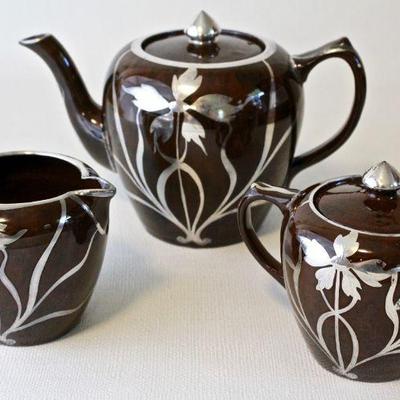Antique ceramic tea pot, sugar, and creamer with silver overlay.